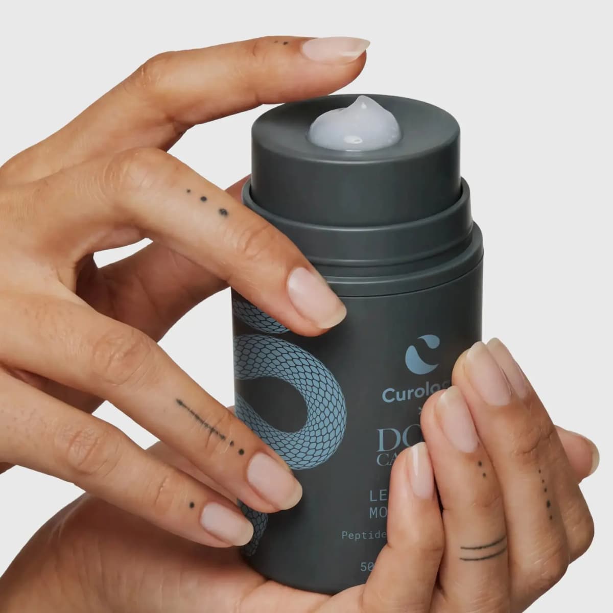Tattooed hands holding the moisturizer jar with a dollop of translucent gel-cream on the pump top