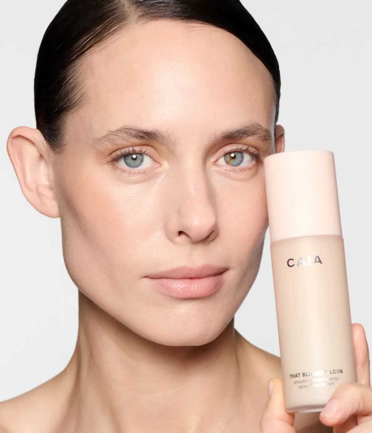 Woman with slicked-back dark hair and smooth, even skin holds CAIA That Blurred Look beside her face