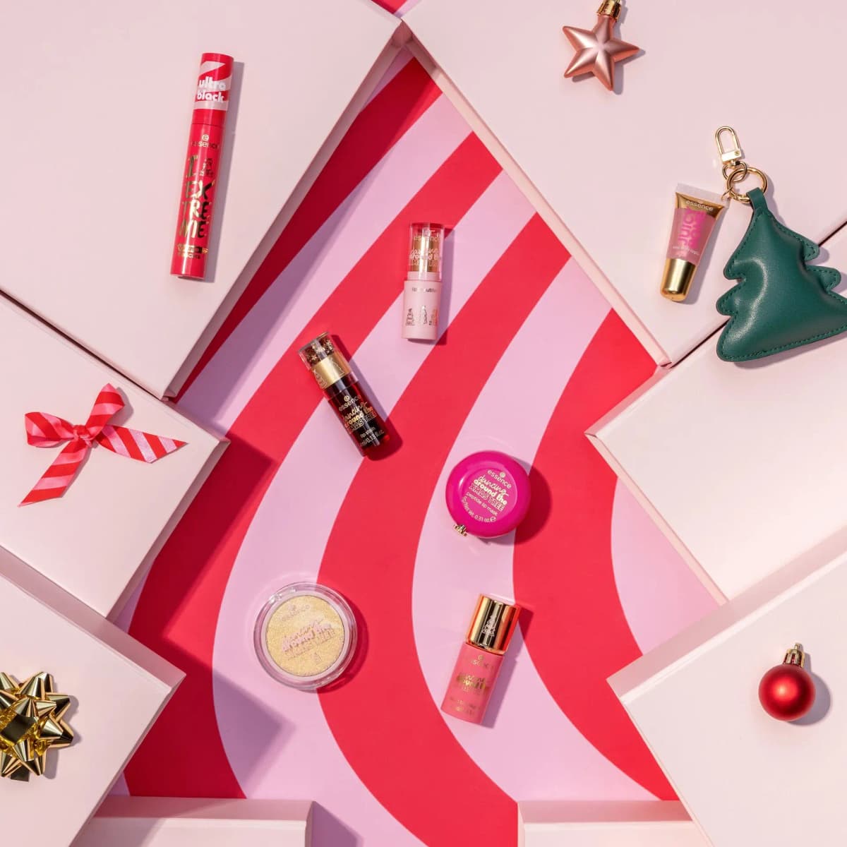 Essence Dancing Around the Xmas Tree Trend Edition makeup laid out on a pink and red striped tree-shaped backdrop with gifts