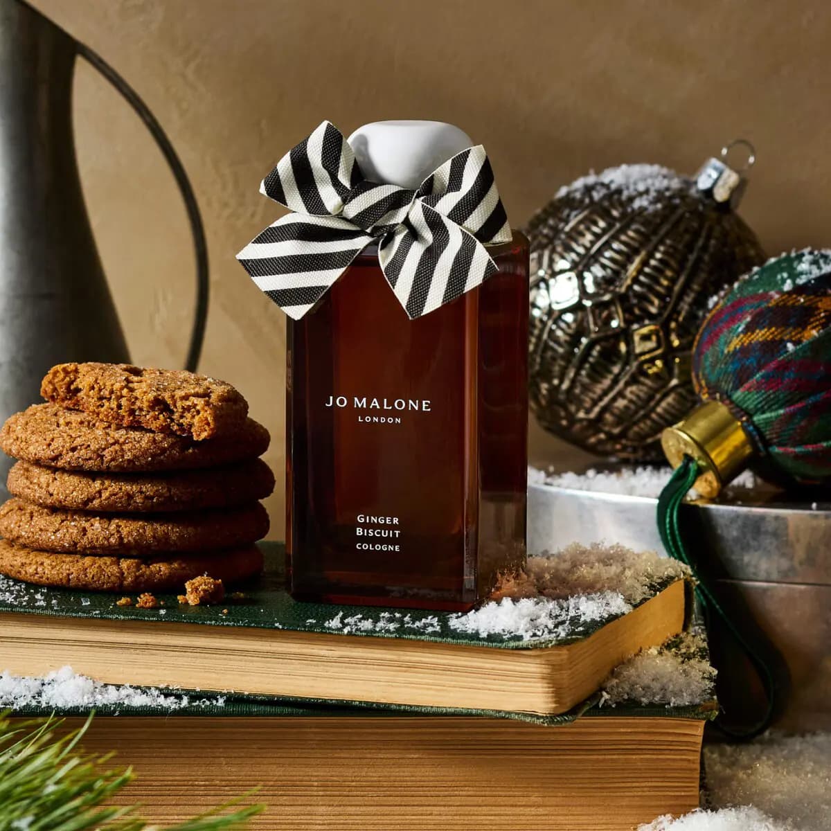 Ginger Biscuit Cologne on stacked green books with stacked ginger cookies, ornaments and faux snow.