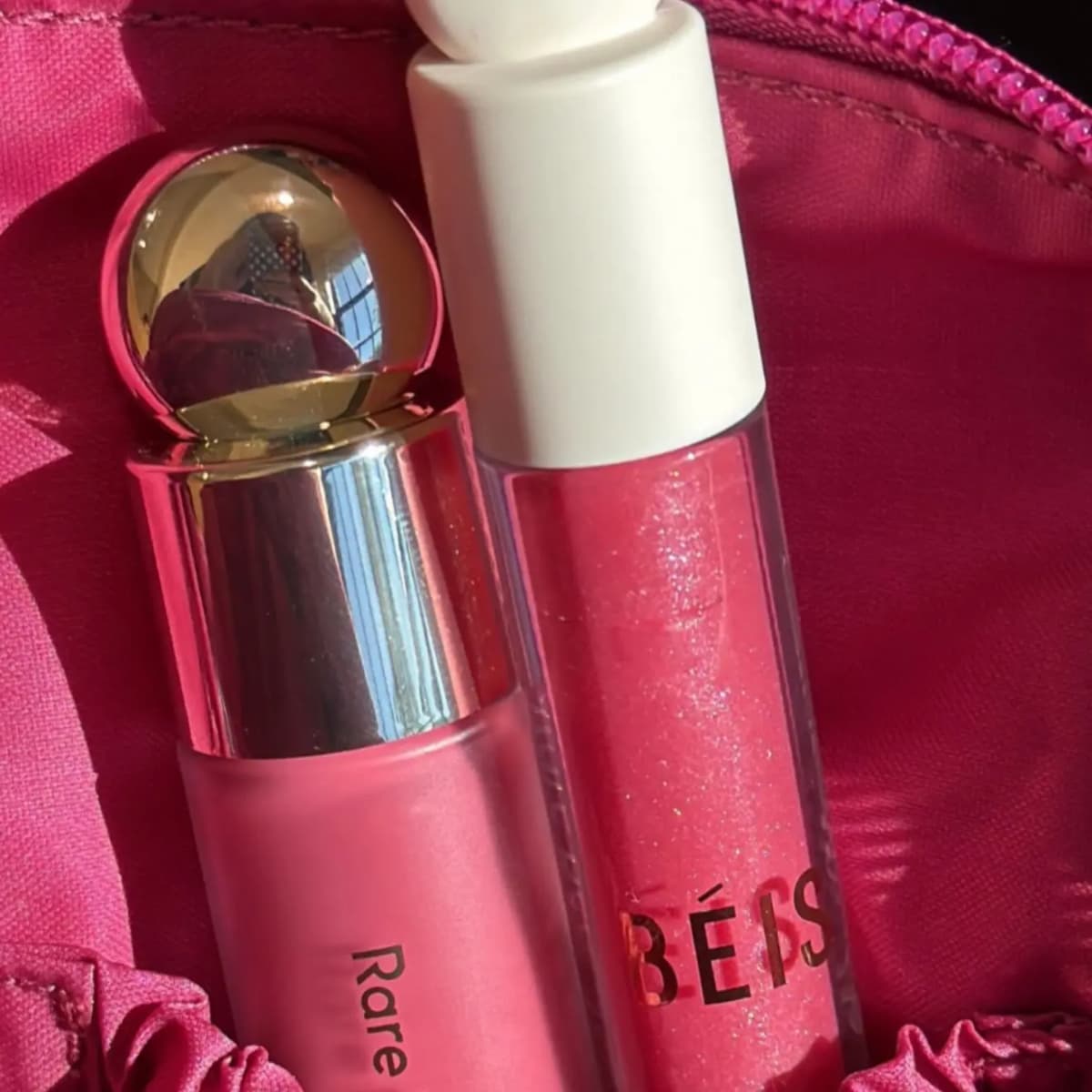 Close-up of the gold-capped blush bottle and sparkly BÉIS gloss tube inside a pink satin-lined pouch