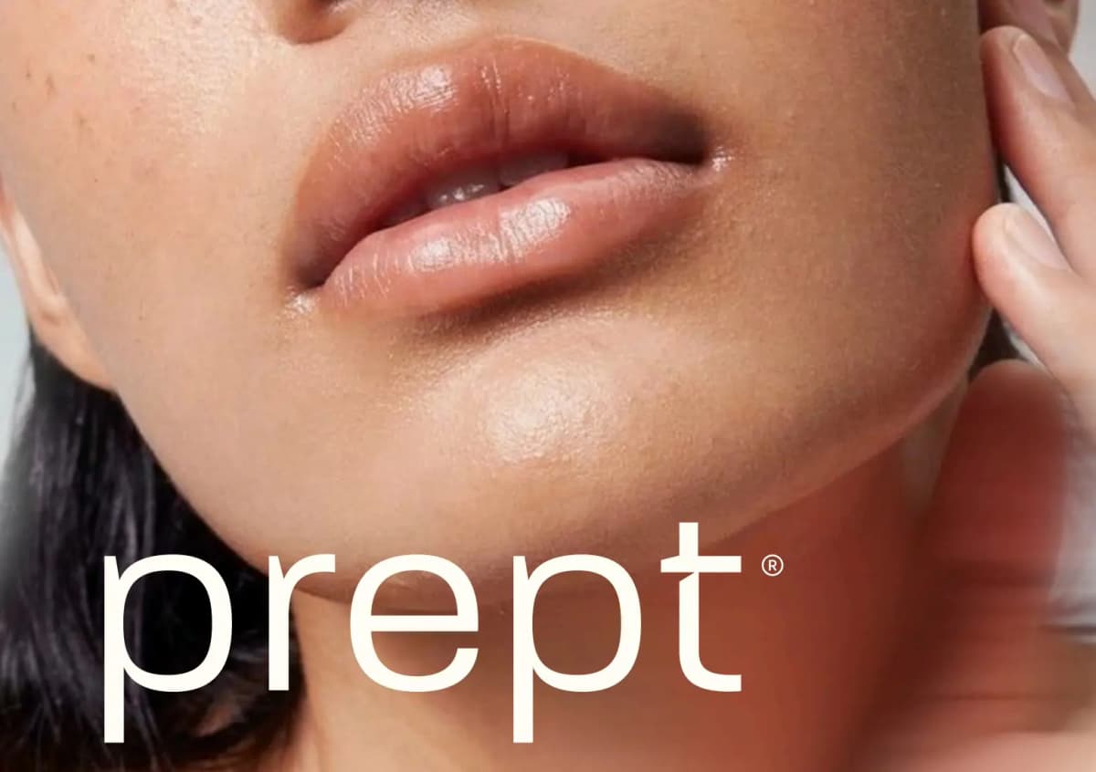 Close-up of glowing skin, glossy lips and jawline with a large cream prept logo overlaid across the chin and neck