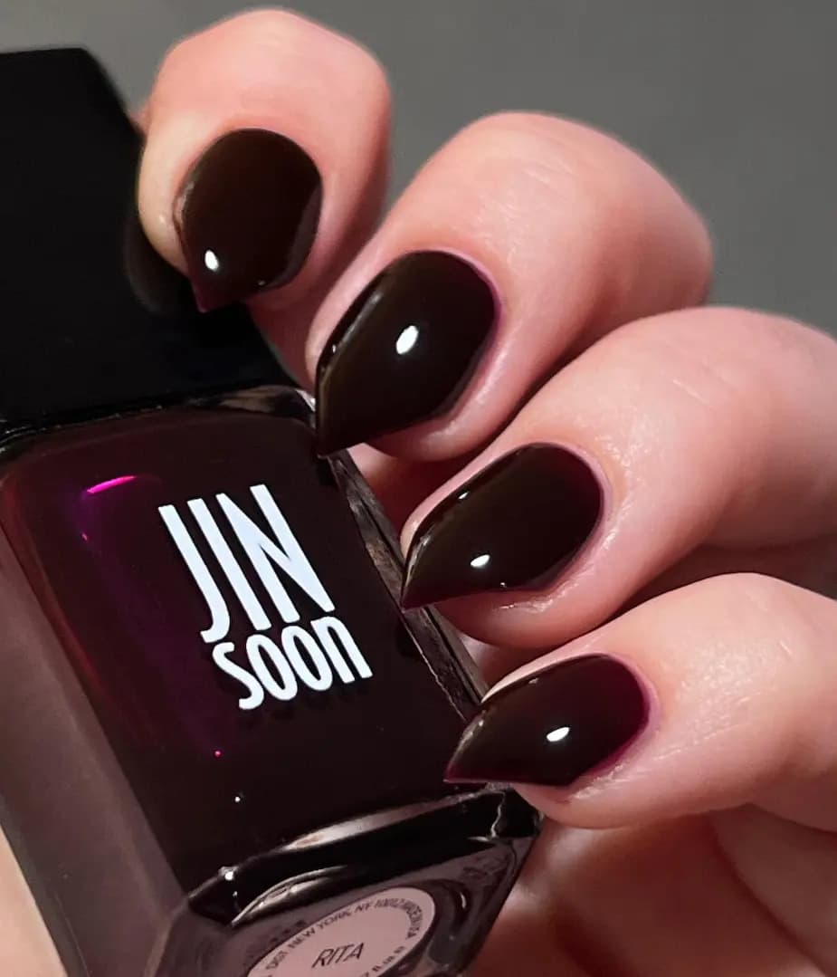 Hand with glossy near-black plum nails holding a JINsoon bottle labelled Rita
