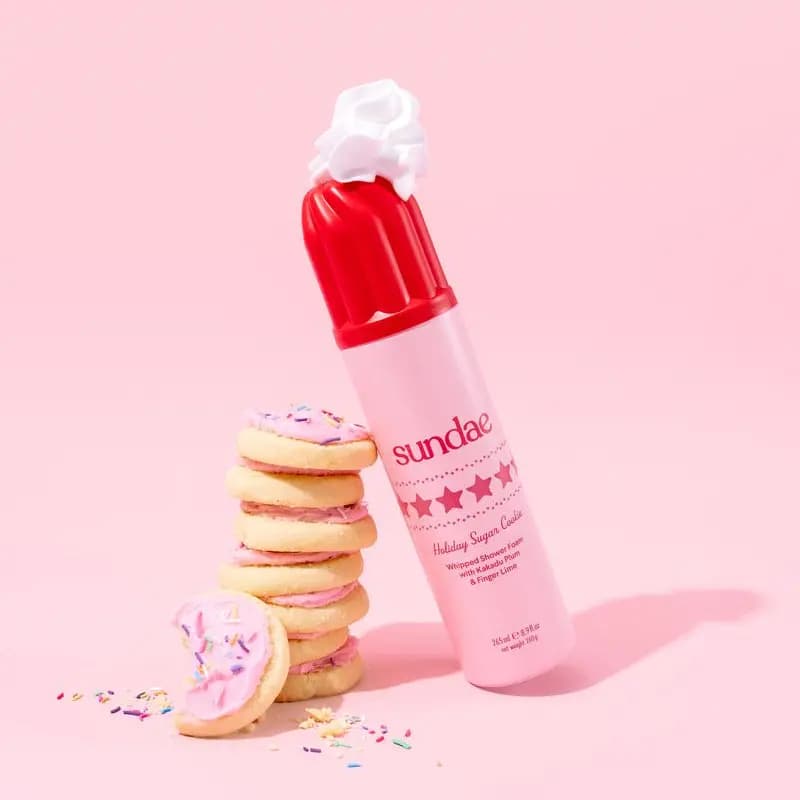 Holiday Sugar Cookie can topped with foam leaning on a stack of pink-frosted sugar cookies