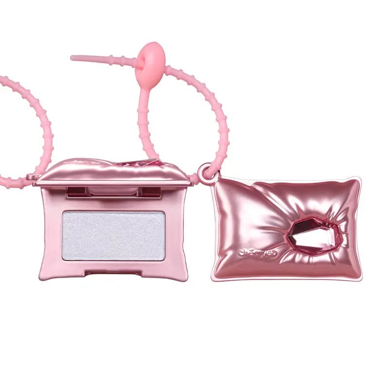 Pink pillow case open to show silvery-white cream highlighter next to the closed case with its pink gem