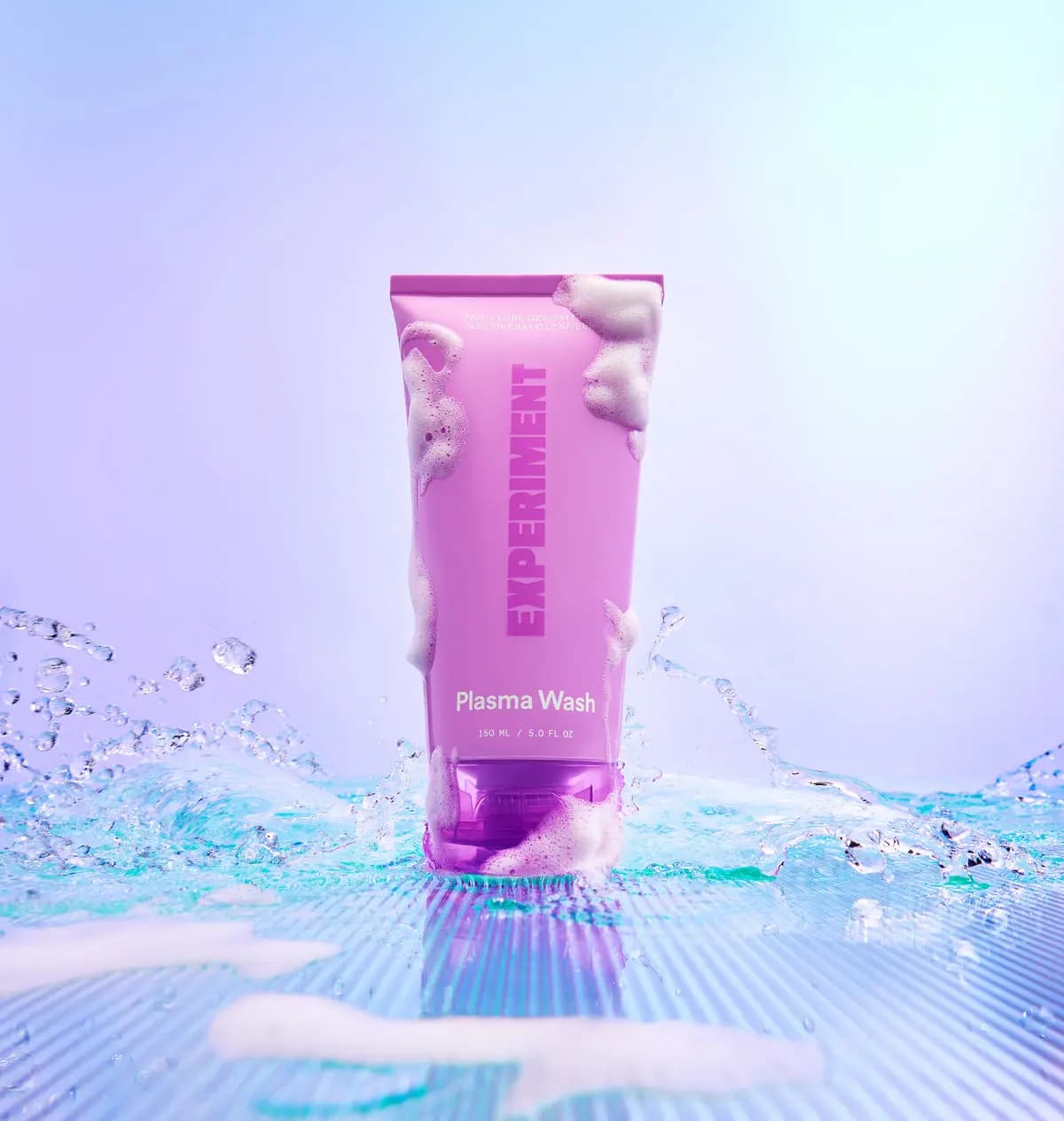 Pink Plasma Wash 150 ml cleanser tube covered in foam, standing in splashing water on an iridescent surface