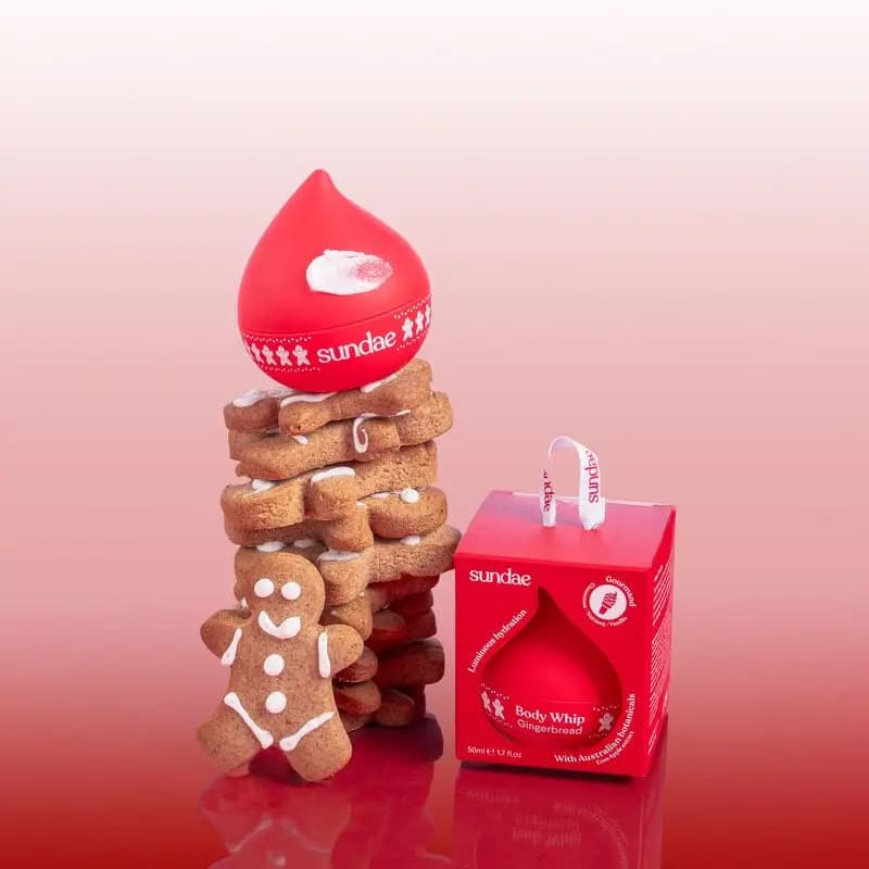 Red Gingerbread Body Whip drop jar atop stacked gingerbread cookies beside its boxed ornament packaging