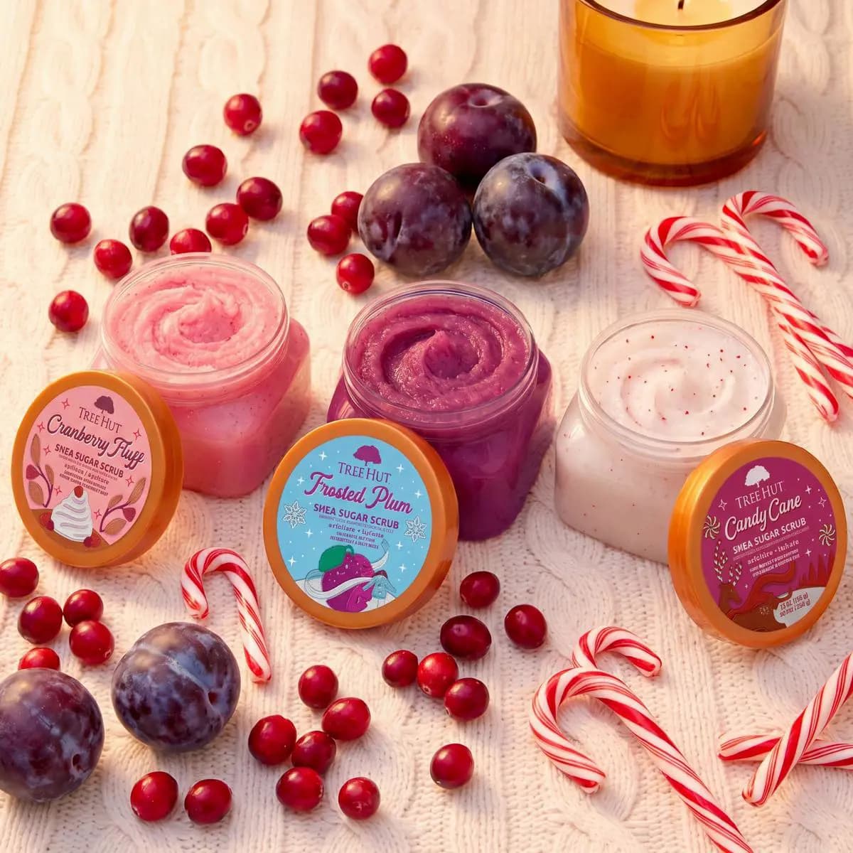 Three open scrub jars showing pink, purple, and white swirled textures with cranberries and candy canes scattered around