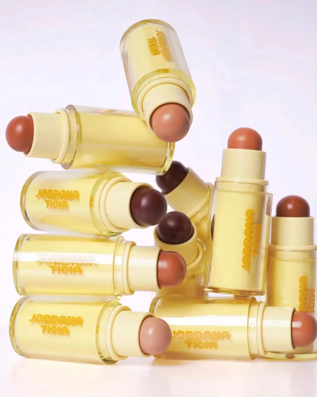 Jordana Ticia Sunny Sticks cream bronzer sticks stacked in pale-yellow tubes, domed bullets from light beige to deep brown