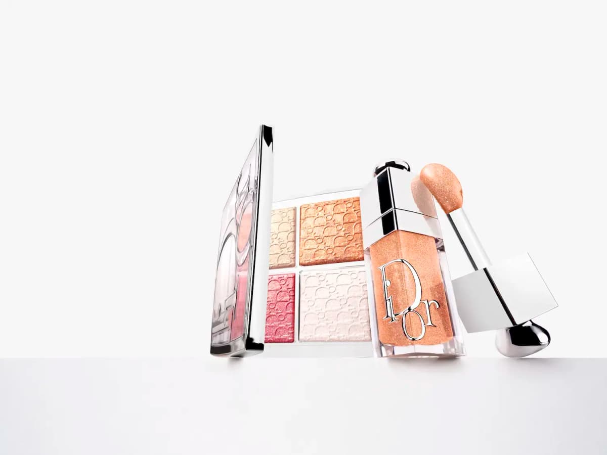Open Dior glow palette in gold, peach, pink and white beside a shimmering peach-gold Dior lip oil and its wand