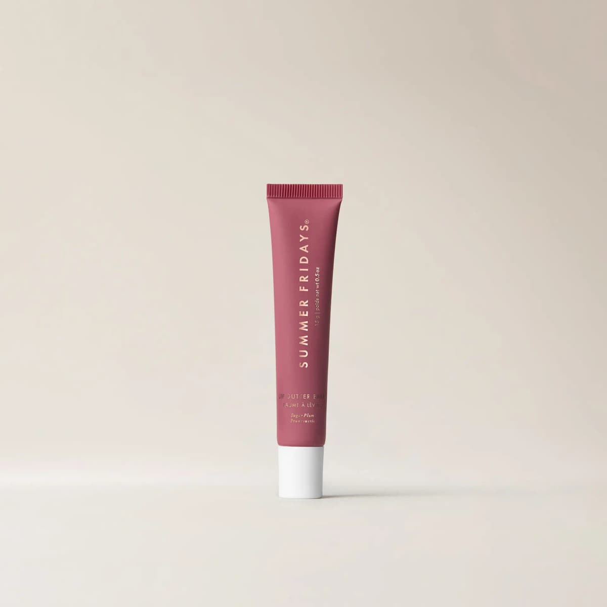 Matte plum Sugar Plum Lip Butter Balm tube with white cap standing on a plain cream background