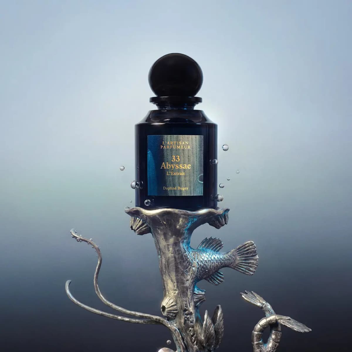Abyssae L'Extrait bottle on a silver sculpture of a fish and tendrils, with water bubbles against a misty blue backdrop