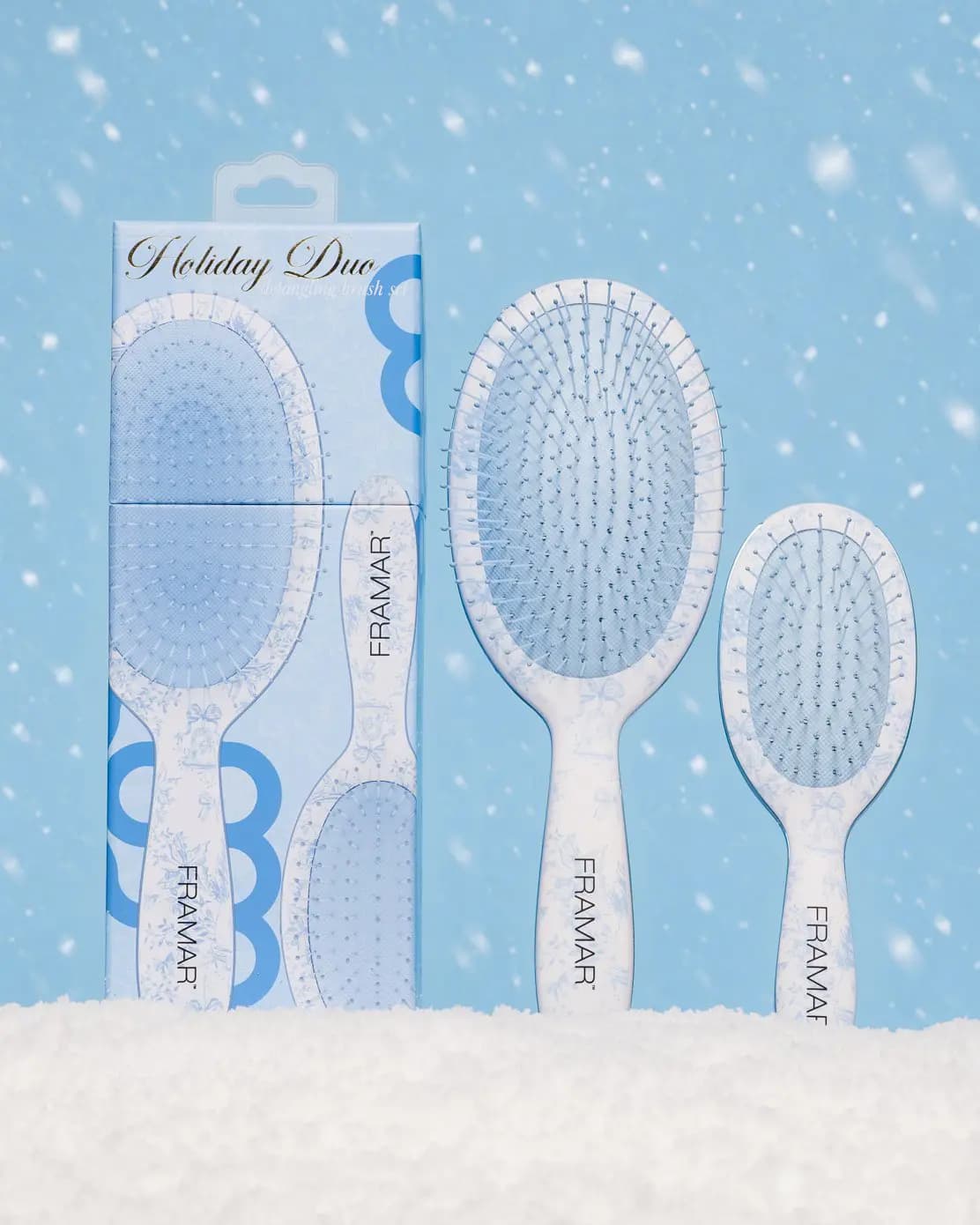 FRAMAR Holiday Duo box and both brushes standing in snow against a light-blue sky with falling snowflakes