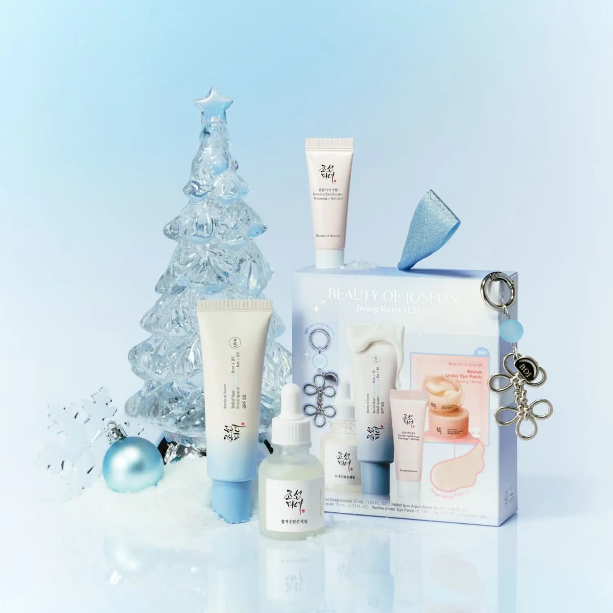 Gift set styled with an ice-clear Christmas tree, blue bauble and snow, eye serum tube perched on the box