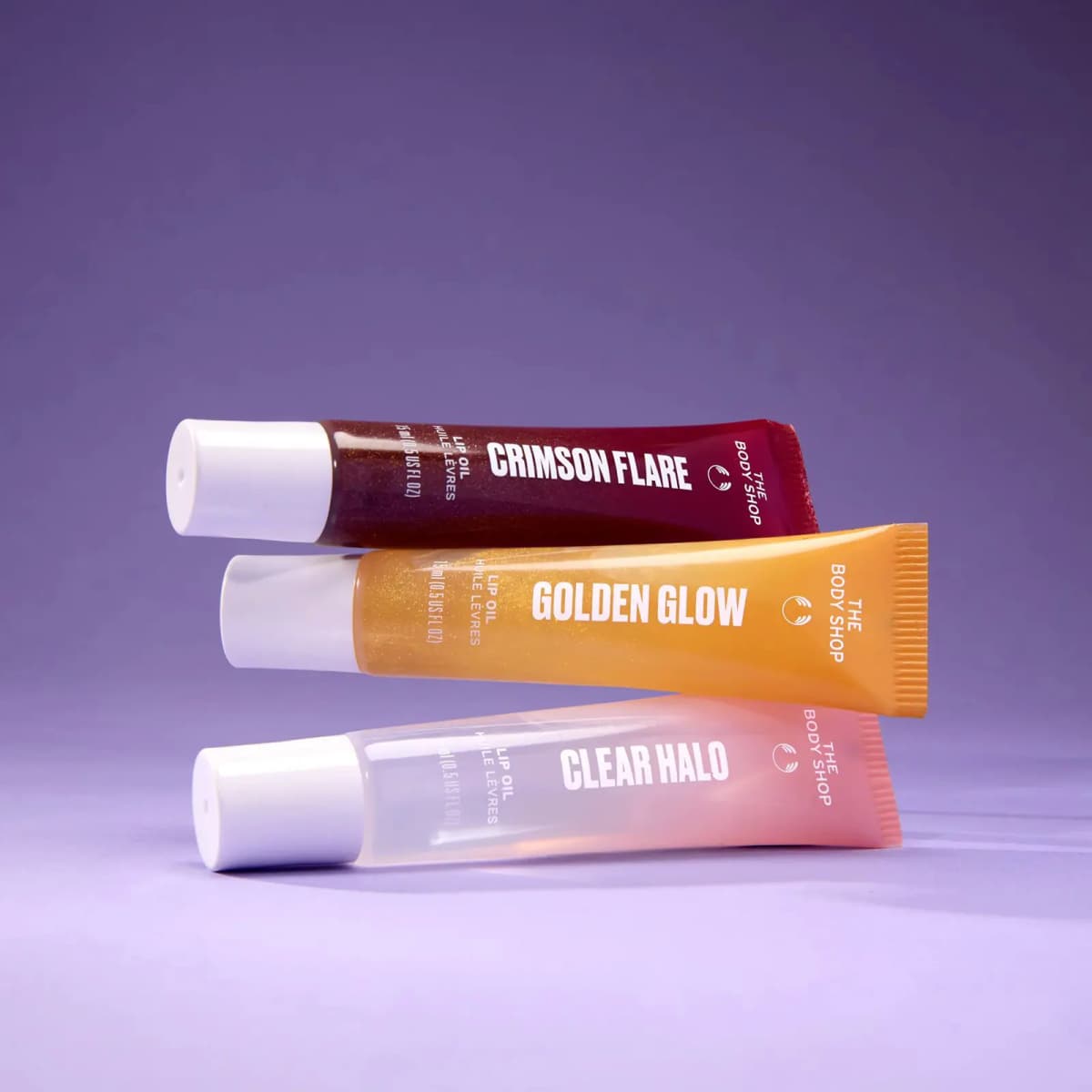 Crimson Flare, Golden Glow and Clear Halo lip oil tubes stacked on a purple background