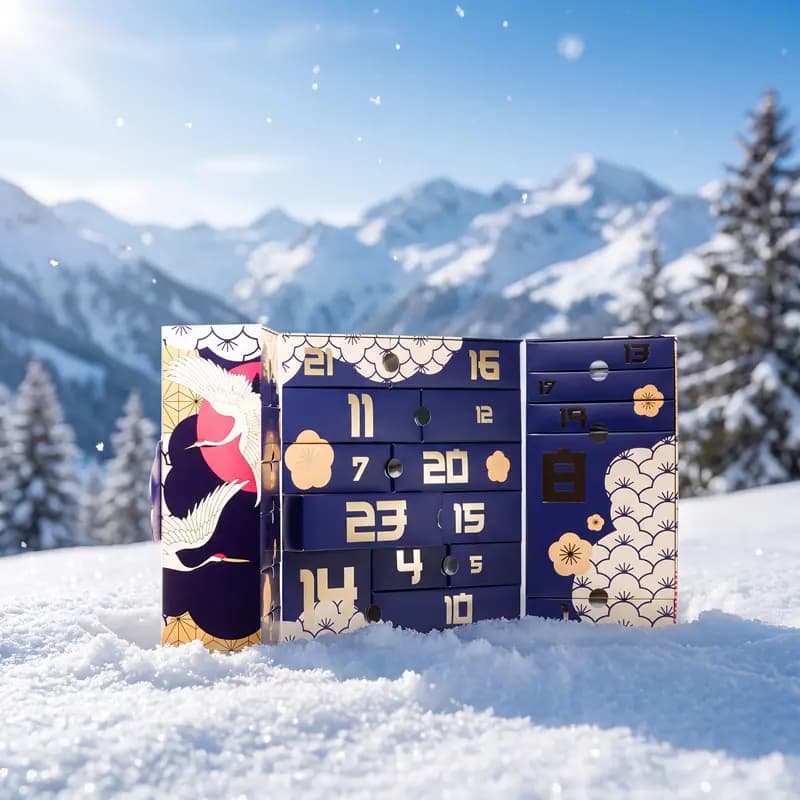 Open navy Japanese-style calendar with gold numbered drawers and crane artwork standing in snow before mountains
