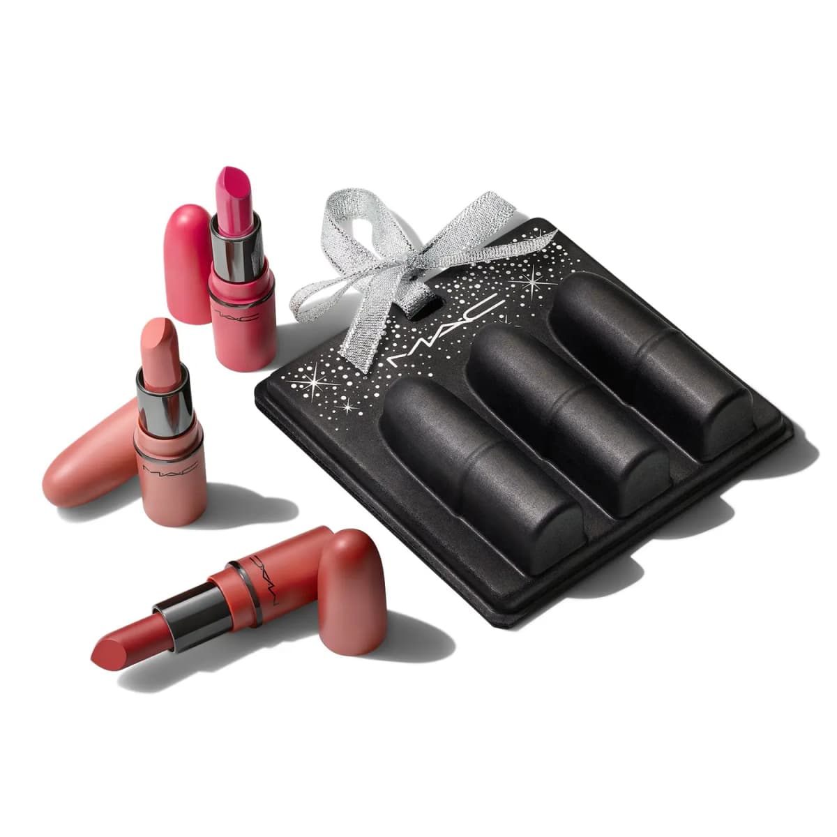 Three uncapped mini lipsticks in pink, nude and brick red laid beside the black case tied with a silver bow