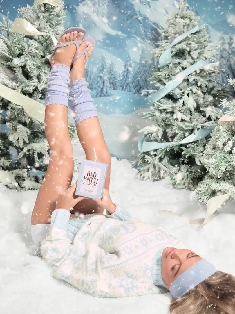 Model lying in snow with legs raised in blue leg warmers, holding an Iced Gumdrop Bad Bitch Energy pack.
