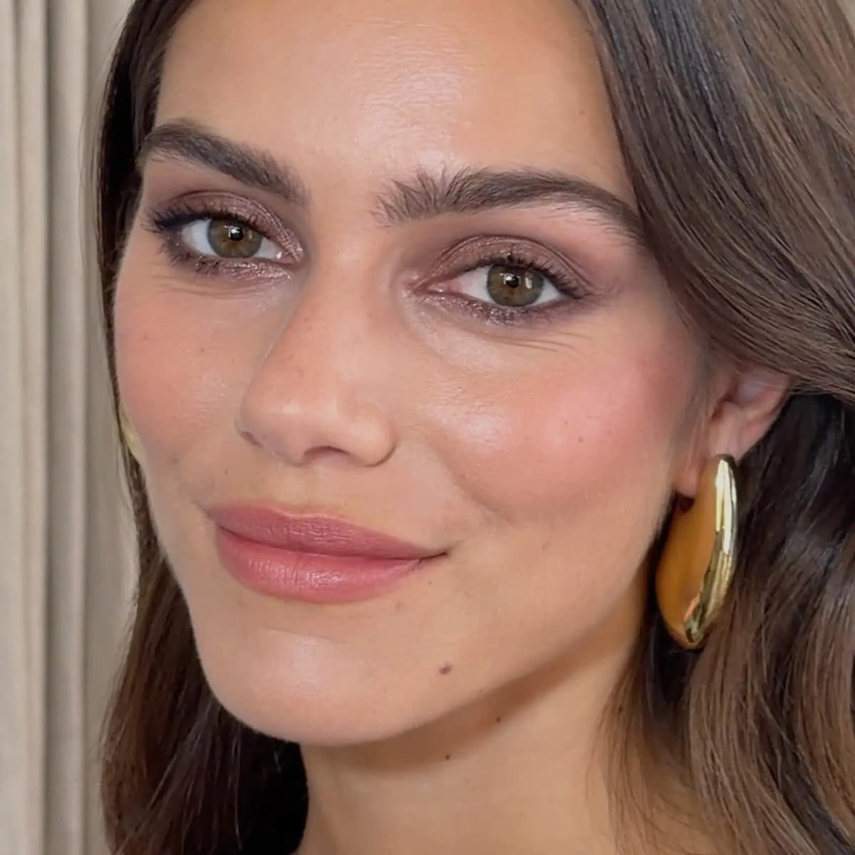 Model with hazel eyes wears smoky taupe shimmer liner, pink blush, nude lips and a gold earring