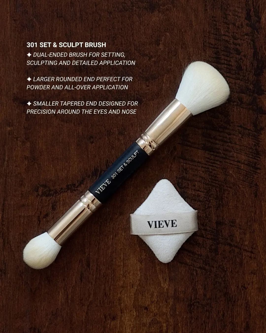 Dual-ended VIEVE 301 Set & Sculpt brush with gold ferrules beside a white diamond-shaped puff on dark wood