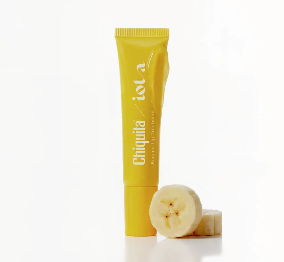 Capped yellow tube smeared with clear golden gloss beside two fresh banana slices on a white surface