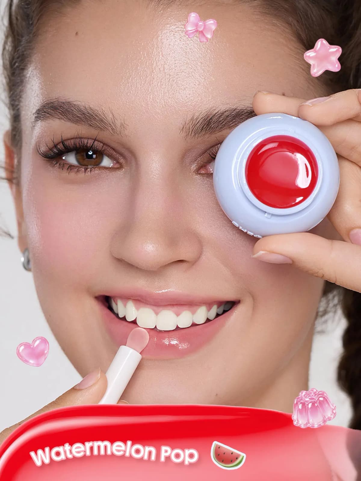 Smiling model holds an open red lip mask pan over one eye while applying it with a wand, labelled Watermelon Pop
