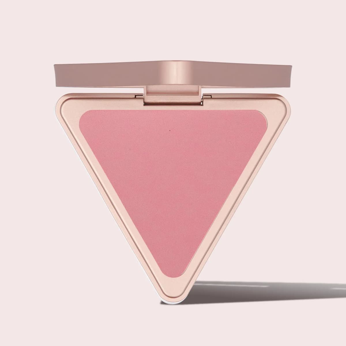Open triangular rose-gold compact with a matte pink pressed powder pan on a pale pink background